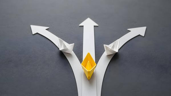 Decision making concept showing a yellow paper boat taking a direct path while others diverge.