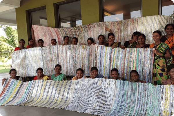 Group of women artisans sitting outdoors, smiling and engaging in traditional handicraft work