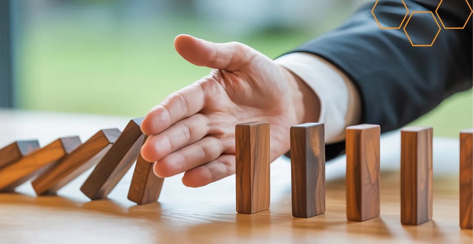 A hand stopping a row of dominoes from falling, illustrating the prevention of inventory errors.