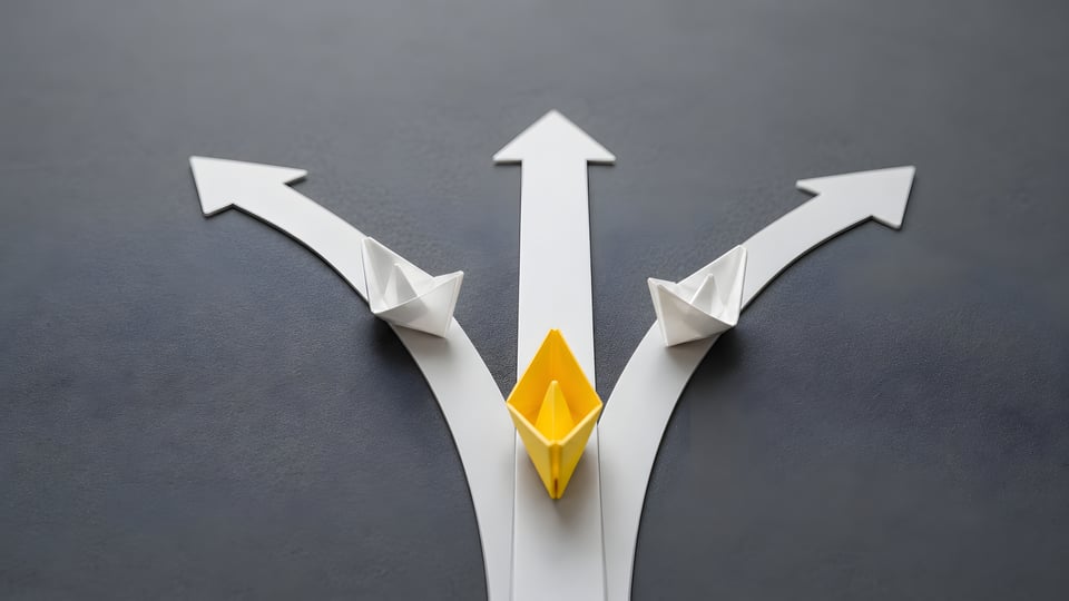 Decision making concept showing a yellow paper boat taking a direct path while others diverge.