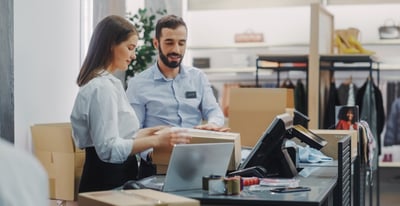 Two store associates packing online orders at a checkout counter, a ship from store order fulfillment strategy